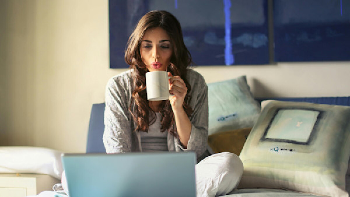 Woman drinking coffee and using her laptop from the bed