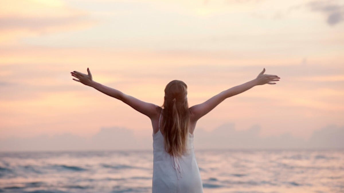 Woman With Arms Raised at Beach During Sunset