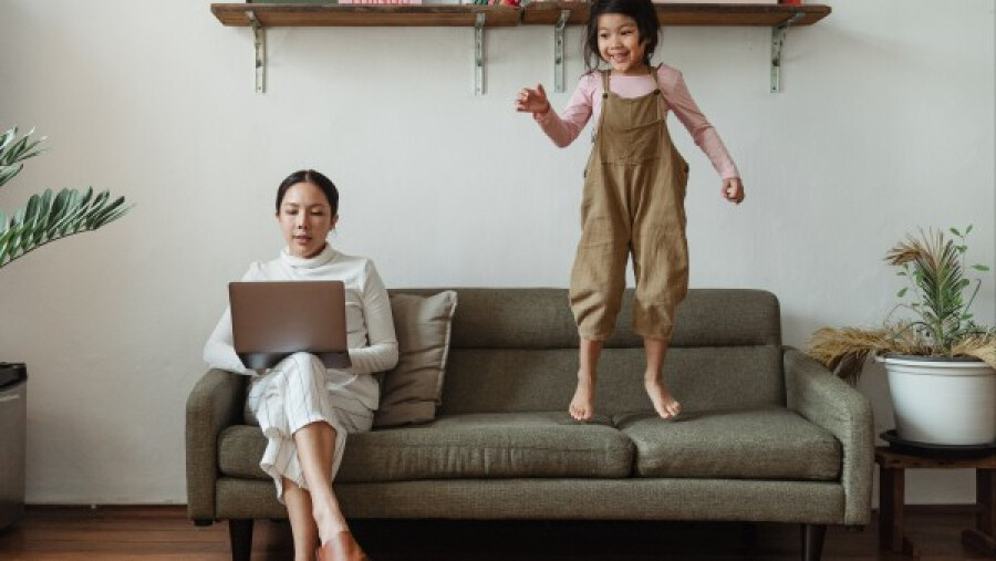 Focused mother working on a laptop near distracting daughter