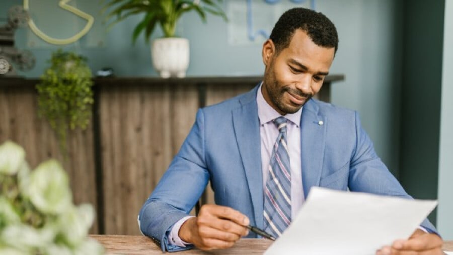 Man in a blue suit holding white paper and a pen