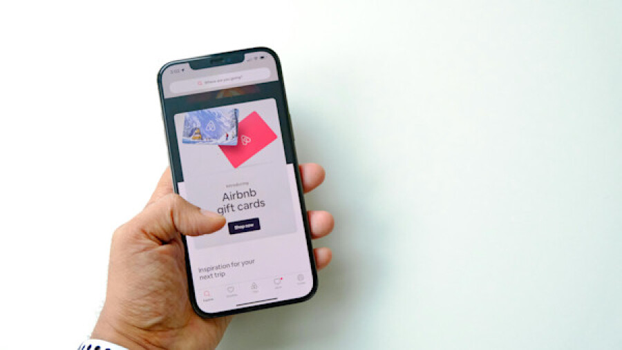 Close-up of a Man Holding a Smartphone Displaying a Shop with Airbnb Gift Cards