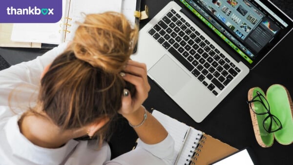woman sat at desk with head in her hands - with thankbox logo