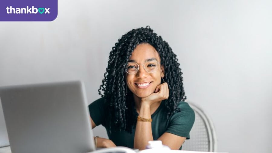 Happy ethnic woman sitting at table with laptop
